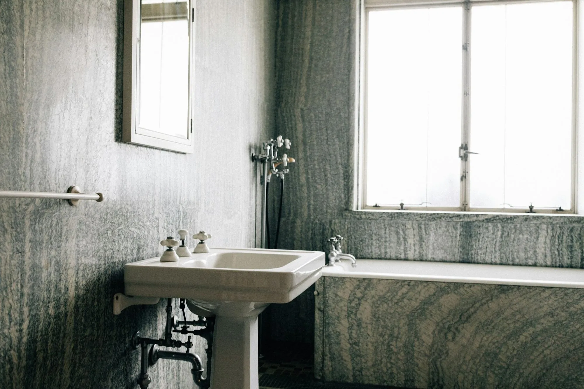 A comparable bath before a remodel, with a pedestal sink and a tub set against stone tiled walls