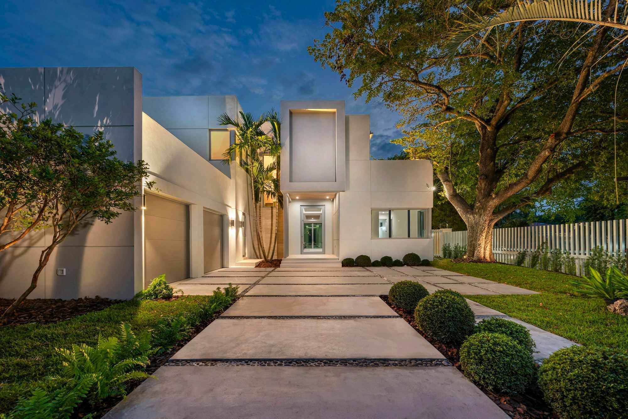 White modern house with an illuminated entry walk at dusk