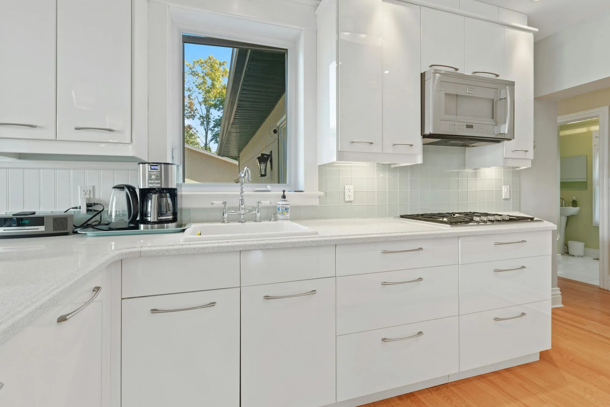 A finished kitchen with white shaker cabinetry and a marble backsplash around the sink window